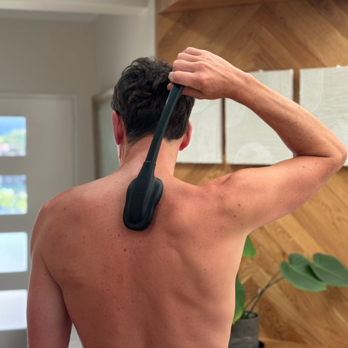 A man using a brush to scratch his back, demonstrating the effectiveness of a back scratcher for relief.